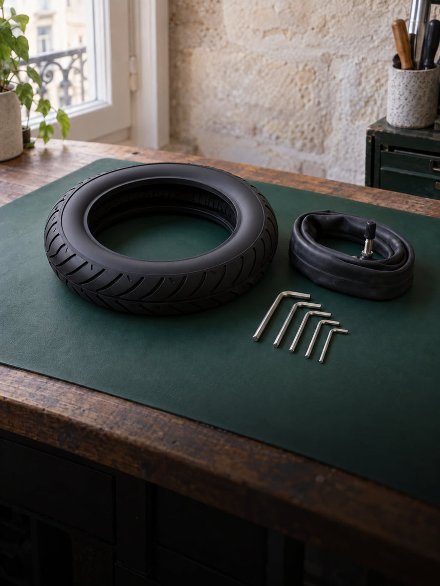 Pneu, chambre à air et clés Allen rangés sur un tapis vert d'établi, à la lumière du jour